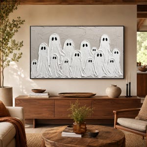 May include: A rectangular wall art piece featuring a textured light gray background with a group of white ghost figures painted in a thick impasto style. Each ghost has two simple black oval eyes. The artwork is enclosed in a thin black frame.