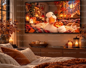 Peut inclure: Un écran de télévision fixé au mur affiche une illustration numérique d'un canard blanc tenant une petite citrouille lumineuse, entouré de feuilles d'automne, de citrouilles, de lanternes et d'un chat endormi dans un décor saisonnier chaleureux.