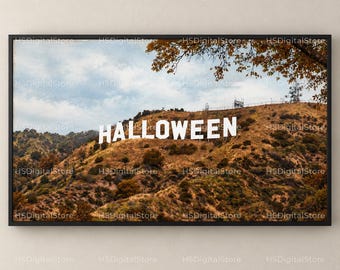 May include: A framed wall art print featuring a hillside landscape with large white capital letters spelling HALLOWEEN. The scene depicts a dry, grassy slope under a cloudy sky, with tree branches visible at the top of the frame.