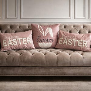 May include: A button-backed, velvet sofa with three Easter-themed cushions. Two cushions have the words "happy EASTER" embroidered in white. The central cushion features bunny ears and the word "Easter".