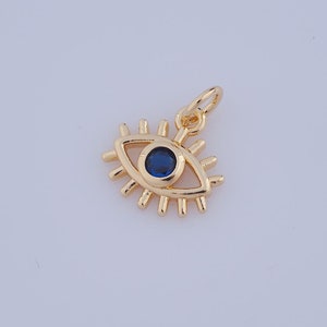 May include: Gold evil eye charm with a blue center. The charm has a detailed design with a circle in the center and rays emanating from the sides.