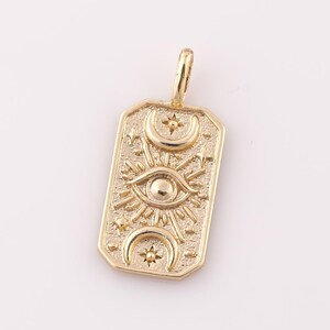 May include: Gold pendant charm with a rectangular shape and an intricate design featuring a sun, moon, and eye motif.