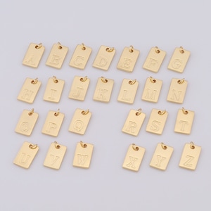 May include: Gold-toned alphabet letter charms, each charm is a rectangular shape with a letter engraved on it. The letters are A through Z.