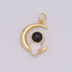 May include: Gold charm featuring a white astronaut with a black helmet sitting on a crescent moon.