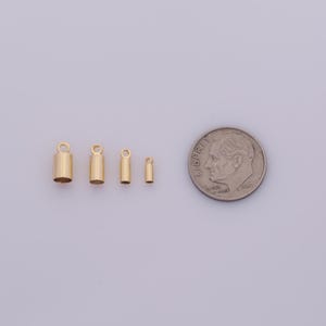 May include: Four gold-colored cylindrical jewelry findings with a loop at the top, next to a U.S. dime for size comparison. The findings vary in size, with the largest measuring approximately 0.3 inches in height.