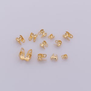 Puede incluir: Una colección de terminales de crimpado dorados, utilizados en la fabricación de joyas. Los terminales son de varios tamaños y formas, con un acabado metálico brillante. Están diseñados para asegurar los extremos de cordones o cadenas.