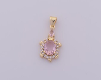May include: A gold-colored pendant featuring a pink oval gemstone surrounded by small clear stones. The pendant has a turtle-like design with a small pink gemstone above the main stone. The pendant is on a white background.