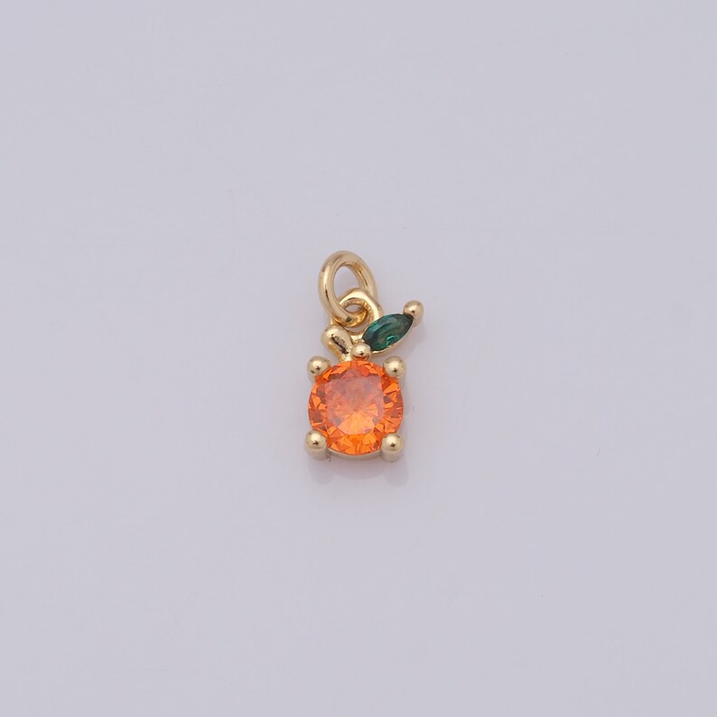 Op de afbeelding: Gouden bedel met een ronde, oranje kristal en een groen blaadje. De bedel is perfect om een ​​toets van whimsy toe te voegen aan sieraden.