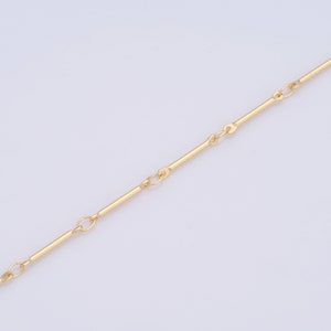 Könnte beinhalten: Eine goldene Kettenkette mit einem schlichten, minimalistischen Design. Die Kette besteht aus dünnen, geraden Stäben, die durch kleine, runde Glieder verbunden sind.