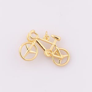 May include: A gold-colored bicycle charm with a detailed design. The bicycle has a classic frame, wheels with star-shaped spokes, a seat, and handlebars. The charm is likely made of metal and is suitable for jewelry making or crafting.
