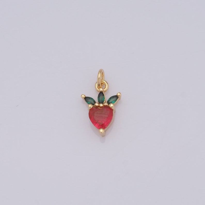 Op de afbeelding: Gouden hangerbedel met een rood hart en groene bladeren.