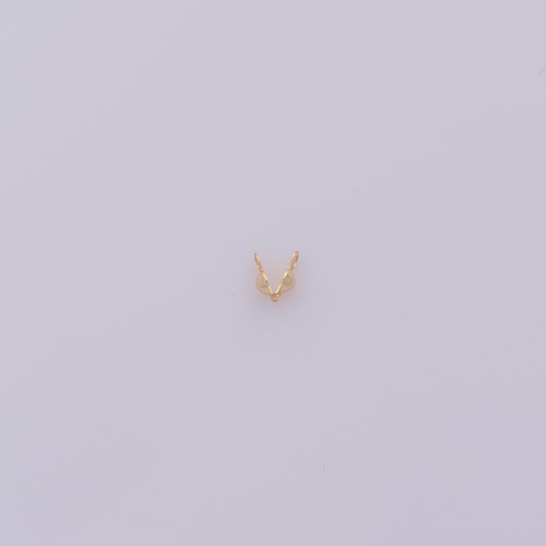 Peut inclure: Un petit &eacute;l&eacute;ment de bijouterie dor&eacute;, probablement une b&eacute;li&egrave;re ou un connecteur, sur fond blanc uni. La pi&egrave;ce a une forme de V avec deux boucles s'&eacute;tendant vers le haut et une petite perle &agrave; la base.