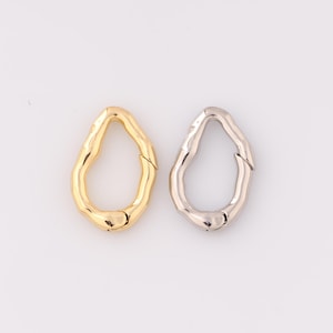 May include: Two metal clasps in the shape of an oval with an irregular, textured surface. One clasp is gold and the other is silver.