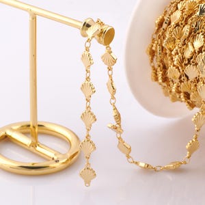 May include: Gold-toned chain with a seashell design. The chain is displayed on a gold-toned stand.