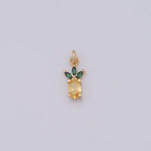 Op de afbeelding: Een gouden ananasbedel met een gele edelsteen en groene kristallen bladeren.