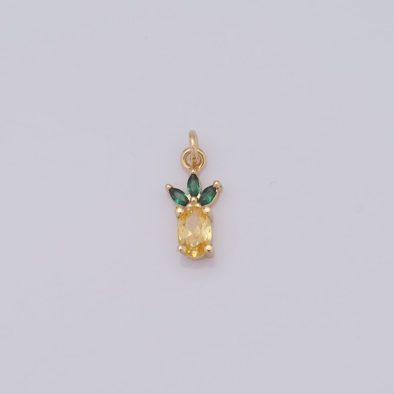 Op de afbeelding: Een gouden ananasbedel met een gele edelsteen en groene kristallen bladeren.