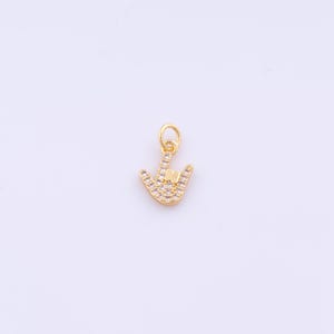 以下が含まれることがあります： 「愛してる」のサインをする手の形をしたゴールドカラーのチャーム。チャームには、小さな透明なクリスタルがちりばめられています。ネックレスやブレスレットに取り付けるための小さなループが上部にあります。