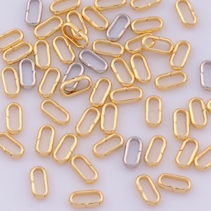May include: A collection of small, oval-shaped metal jump rings scattered across the frame. The majority of these openable links are finished in a polished gold tone, while a smaller number are finished in a polished silver tone.
