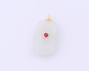 Puede incluir: Un colgante rectangular con forma redondeada, con una fianza dorada y una pequeña gema roja redonda engastada en un bisel dorado. El colgante es de color blanco cremoso.