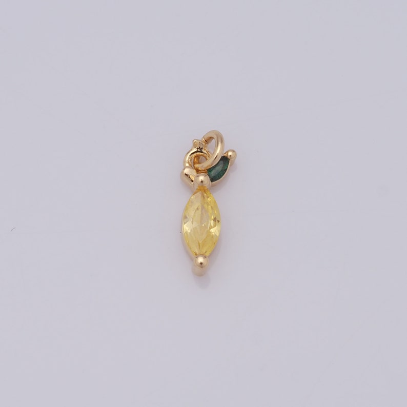 Op de afbeelding: Een gouden bedel met een gele, markiesvormige edelsteen en een groen bladdetail.