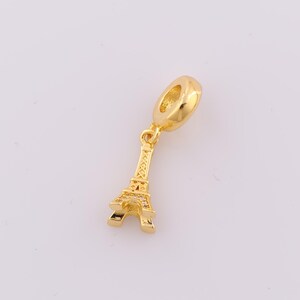 Puede incluir: Encanto dorado con un diseño detallado de la Torre Eiffel con piedras brillantes transparentes. El encanto tiene un bucle redondo para sujetarlo a una pulsera o collar.