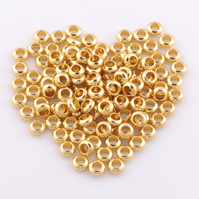 Peut inclure: Une grande collection de petites perles rondes de couleur or m&eacute;tallique. Chaque perle pr&eacute;sente une surface lisse et r&eacute;fl&eacute;chissante avec un trou central, dispos&eacute;es en un tas &eacute;pars. Les perles sont uniformes en forme et en taille, avec une finition polie.