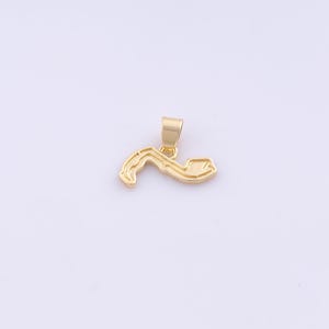 May include: A gold-colored pendant in the shape of a curved object with a rectangular end. The pendant has a small loop at the top for a chain. The background is a plain white.