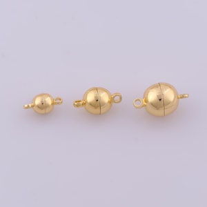 May include: Three gold-colored spherical magnetic clasps of varying sizes arranged in a horizontal row. Each clasp features a smooth, polished surface and two small loops on opposite sides for attachment to jewelry or other craft projects.