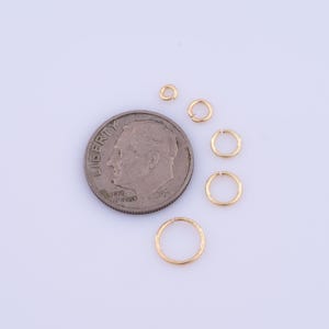 May include: Five gold jump rings of different sizes, next to a US dime coin for scale.