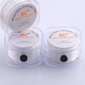 May include: Clear plastic containers holding white stretchy cord. Each container has a label with the text "Rehathan Concept USA" and "RC Strong Stretchy Cord". The labels also indicate the length and wire diameter of the cord.