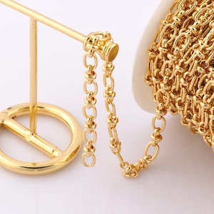 May include: A gold chain with a round link design. The chain is coiled on a spool and a small section is hanging off the spool.