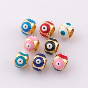 May include: Assortment of colorful evil eye beads with gold accents. Each bead features a different color background with a white eye and black pupil. The beads are round and have a hole in the center for stringing.