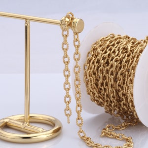Op de afbeelding: Een spoel met een gouden ketting, met een lengte van ketting die er vanaf hangt. De ketting ligt op een gouden standaard.