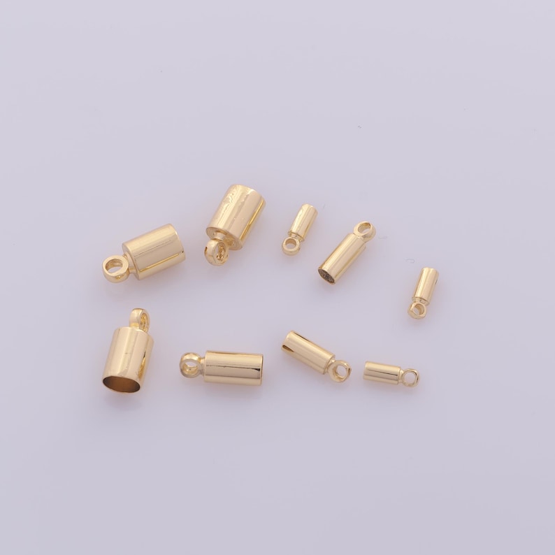 May include: A collection of gold-colored jewelry findings, including various sizes of crimp end caps and tube-shaped components with small loops. These findings are likely used for jewelry making and crafting.