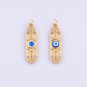 May include: Two gold-colored pendants with an elongated shape. Each pendant features a blue and white evil eye charm, along with decorative crescent moons and stars. The pendants are designed with a loop at the top for hanging.