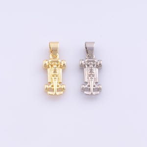 May include: Two pendant necklaces in the shape of race cars. One is gold-colored, and the other is silver-colored. The pendants have a loop at the top for a chain.