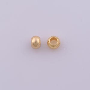 Peut inclure: Deux petites perles rondes de couleur or m&eacute;tallique avec une surface lisse et r&eacute;fl&eacute;chissante. Chaque perle pr&eacute;sente un trou circulaire central, con&ccedil;u pour &ecirc;tre enfil&eacute; sur un cordon ou un fil. Les perles sont identiques en forme et finition.