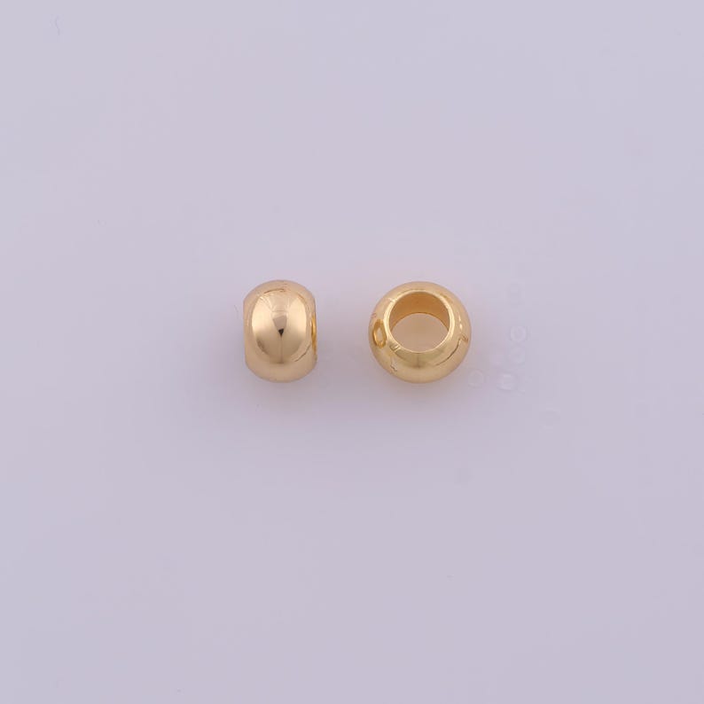 Peut inclure: Deux petites perles rondes de couleur or m&eacute;tallique avec une surface lisse et r&eacute;fl&eacute;chissante. Chaque perle pr&eacute;sente un trou circulaire central, con&ccedil;u pour &ecirc;tre enfil&eacute; sur un cordon ou un fil. Les perles sont identiques en forme et finition.