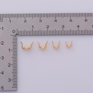 Peut inclure: Quatre appr&ecirc;ts de bijoux dor&eacute;s de diff&eacute;rentes tailles sont dispos&eacute;s sur une surface blanche &agrave; c&ocirc;t&eacute; d'une r&egrave;gle. Les appr&ecirc;ts ont une forme en V avec de petits &eacute;l&eacute;ments d&eacute;coratifs. La r&egrave;gle est gradu&eacute;e en centim&egrave;tres.