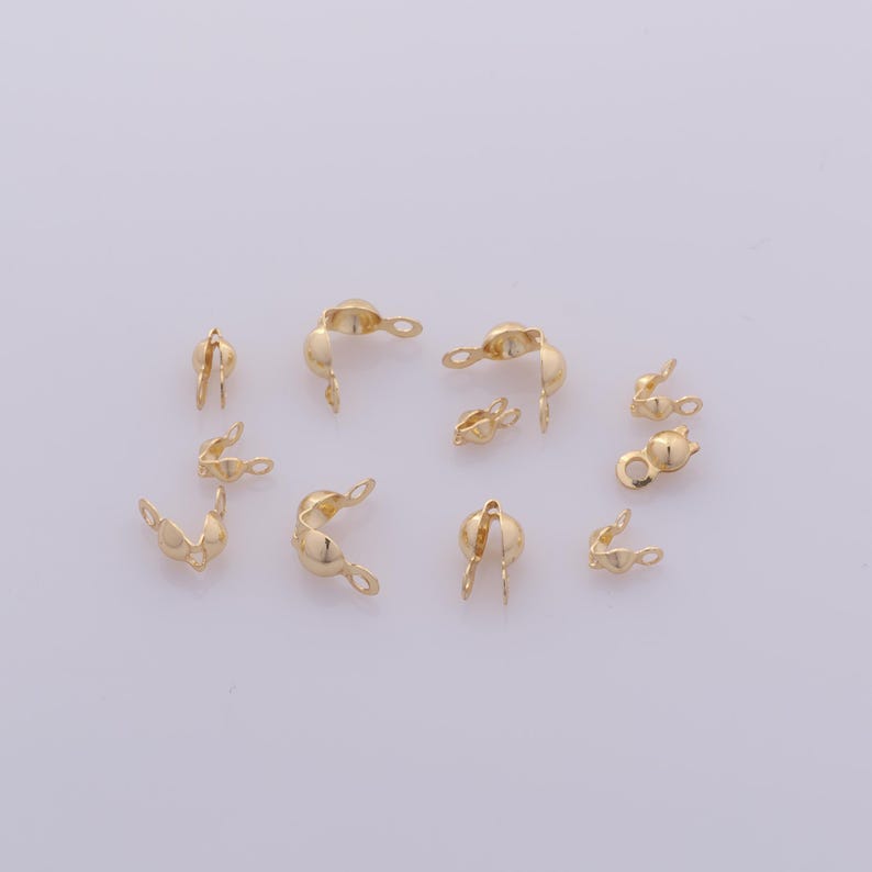 Peut inclure: Une collection de petits embouts &agrave; sertir dor&eacute;s pour la fabrication de bijoux. Ces embouts ont une forme incurv&eacute;e avec une boucle &agrave; une extr&eacute;mit&eacute; et une ouverture fendue &agrave; l'autre, con&ccedil;us pour fixer les extr&eacute;mit&eacute;s des cordons ou cha&icirc;nes de bijoux.