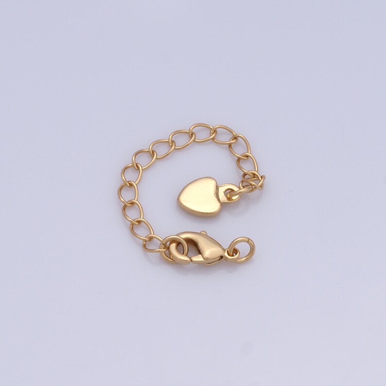 Może przedstawiać: Złoty łańcuszek z zawieszką w kształcie serca i zapięciem typu karabińczyk.