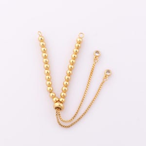 May include: Gold beaded bracelet with a sliding clasp and two clear crystal accents.