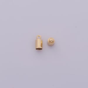 May include: Two gold-colored metal jewelry findings. One is a cylindrical crimp end with a loop, and the other is a small, rounded cap. These findings are used in jewelry making to secure the ends of cords or chains.
