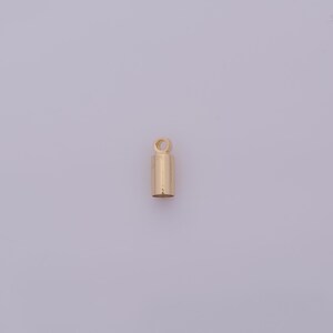 May include: A small, gold-colored cylindrical jewelry finding with a loop at the top. The finding is a simple, minimalist design, likely used for attaching pendants or charms to necklaces or bracelets.