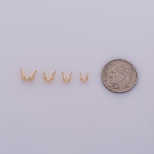 Peut inclure: Quatre petits appr&ecirc;ts de bijoux dor&eacute;s, en forme de mini-soutiens-gorge, sont dispos&eacute;s en rang&eacute;e. Une pi&egrave;ce de 10 cents am&eacute;ricaine est plac&eacute;e &agrave; c&ocirc;t&eacute; des appr&ecirc;ts pour comparaison de taille. Les appr&ecirc;ts ont une finition brillante.