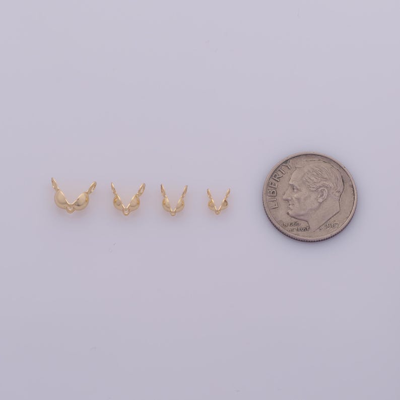 Peut inclure: Quatre petits appr&ecirc;ts de bijoux dor&eacute;s, en forme de mini-soutiens-gorge, sont dispos&eacute;s en rang&eacute;e. Une pi&egrave;ce de 10 cents am&eacute;ricaine est plac&eacute;e &agrave; c&ocirc;t&eacute; des appr&ecirc;ts pour comparaison de taille. Les appr&ecirc;ts ont une finition brillante.