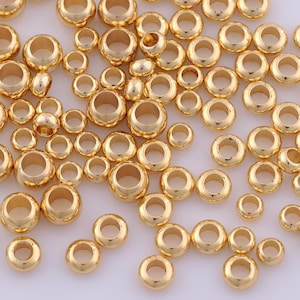 Peut inclure: Une collection de nombreuses perles rondes en or m&eacute;tallique dispers&eacute;es dans le cadre. Chaque perle pr&eacute;sente une surface lisse et polie avec un trou central, variant l&eacute;g&egrave;rement en taille, cr&eacute;ant une apparence uniforme de composants de bijoux dor&eacute;s brillants.