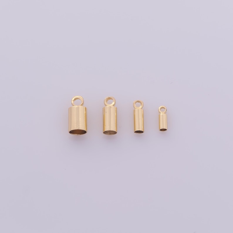 May include: Four gold-colored crimp end caps of varying sizes, each with a small loop at the top. The caps are cylindrical, with a smooth, polished finish. They are arranged horizontally against a plain, light background, suitable for jewelry making.