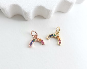 May include: Two rainbow charm pendants, one gold and one rose gold, with colourful gemstones. The charms are shaped like a rainbow arch.