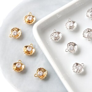 May include: A selection of small, shell-shaped charms. Some are gold-coloured, others silver-coloured, each with a clear, round gemstone in the centre. The charms have a small loop for attaching to jewellery.